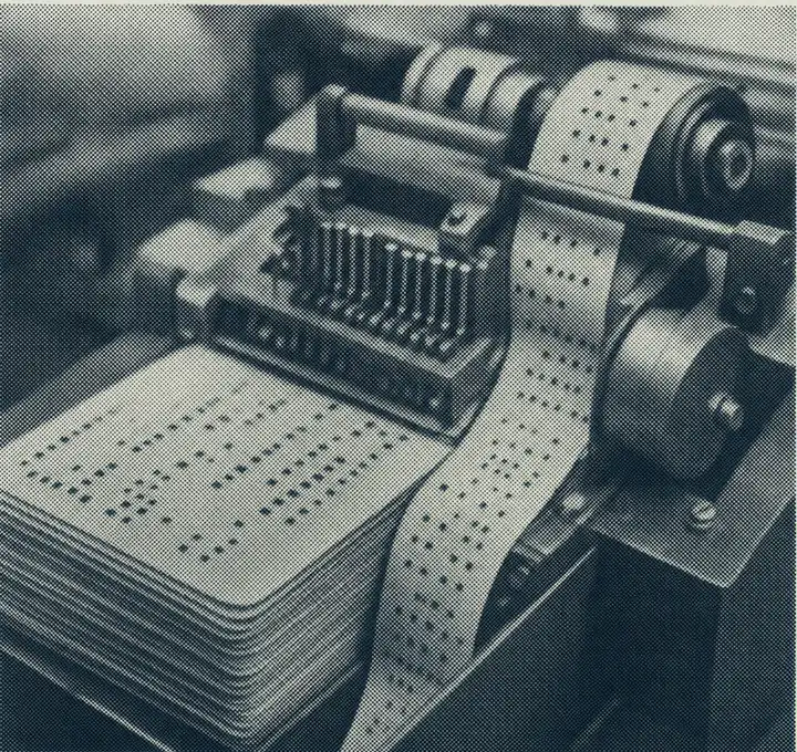 Halftone plate of a punched-card tabulating machine feeding a continuous perforated tape over rollers beside a stack of finished cards.